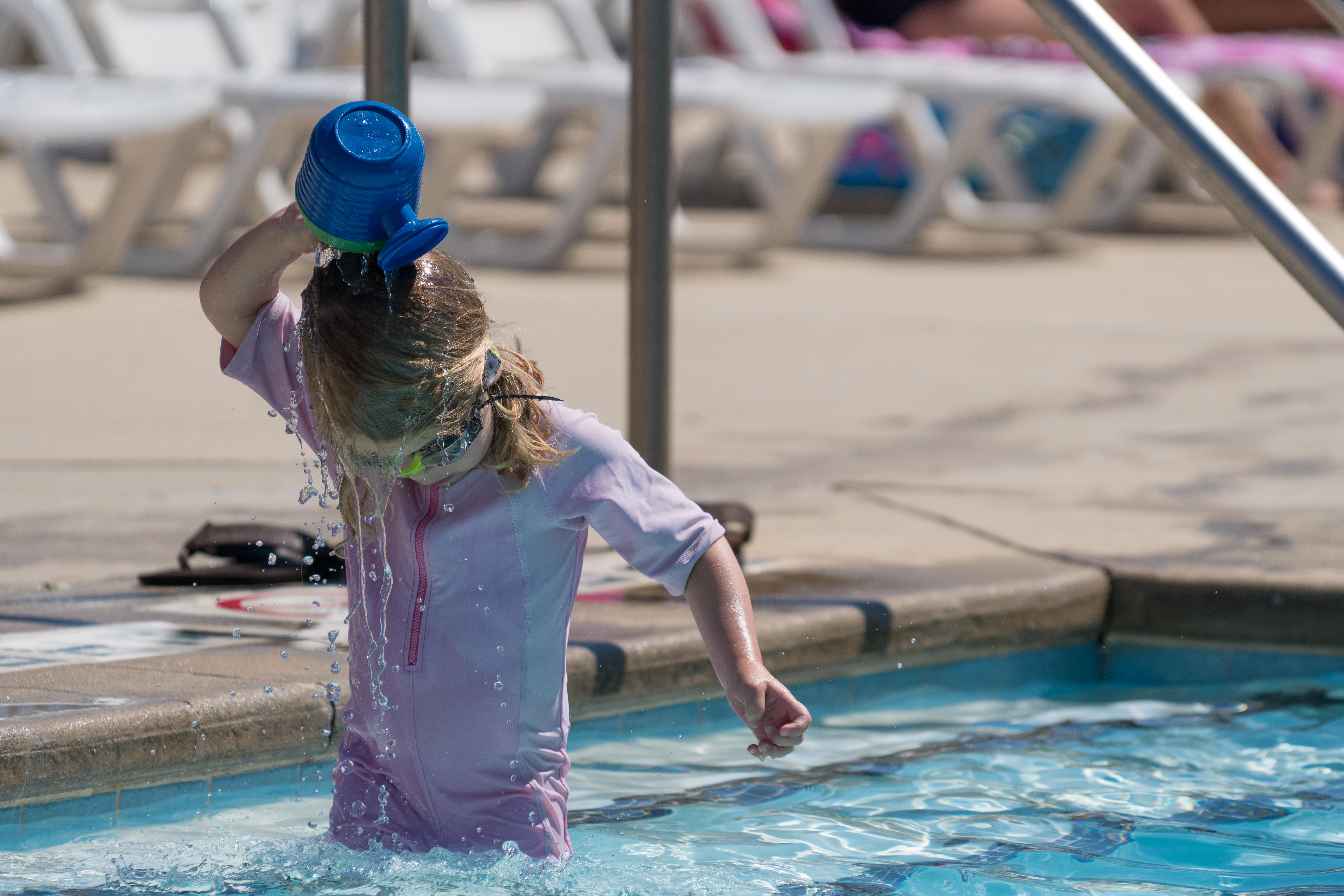 little girl pouring water on head in pool