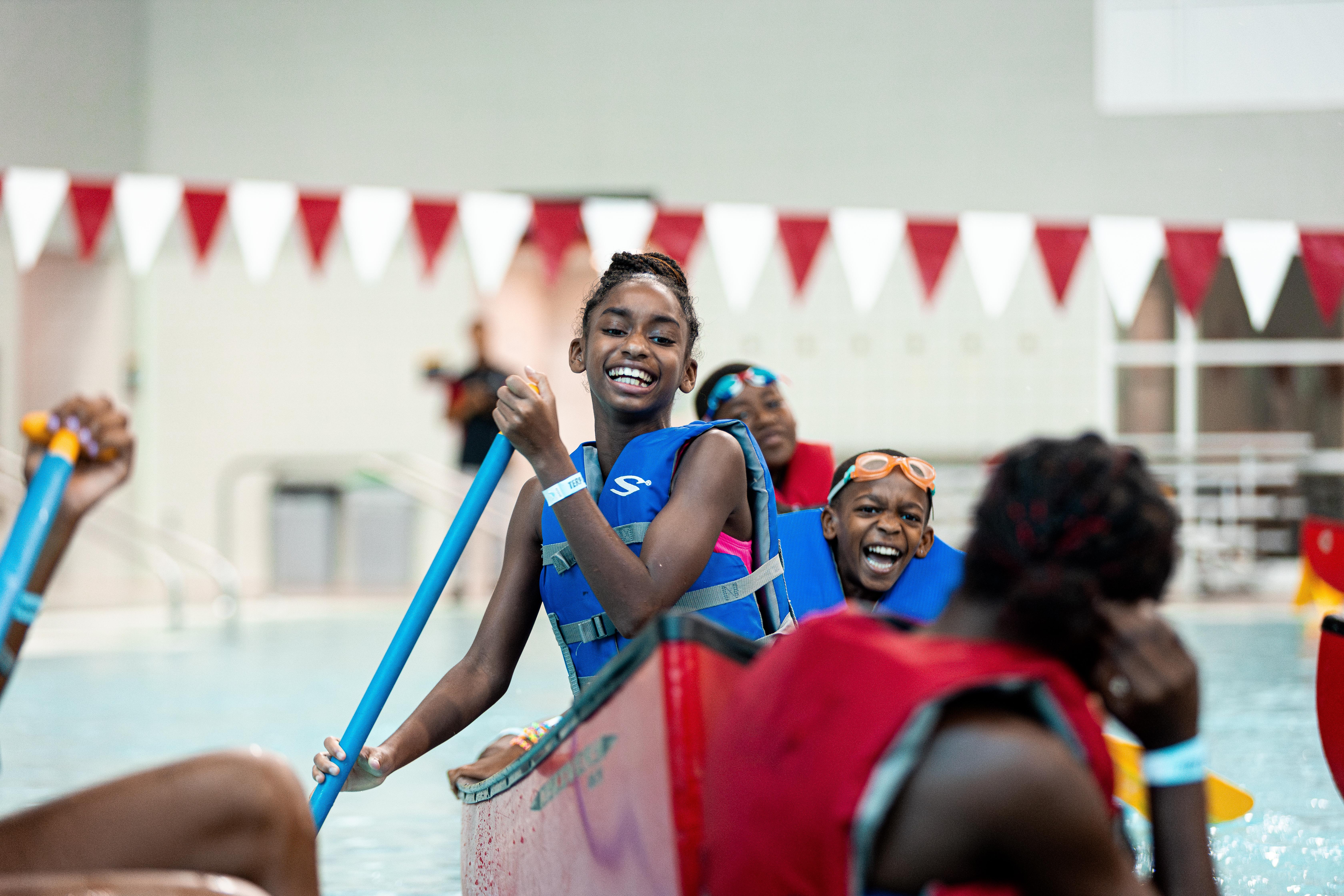 Two campers smiling while paddling in a canoe in the pool